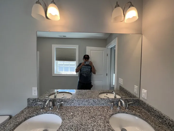Frameless mirror above a granite double vanity with sconces