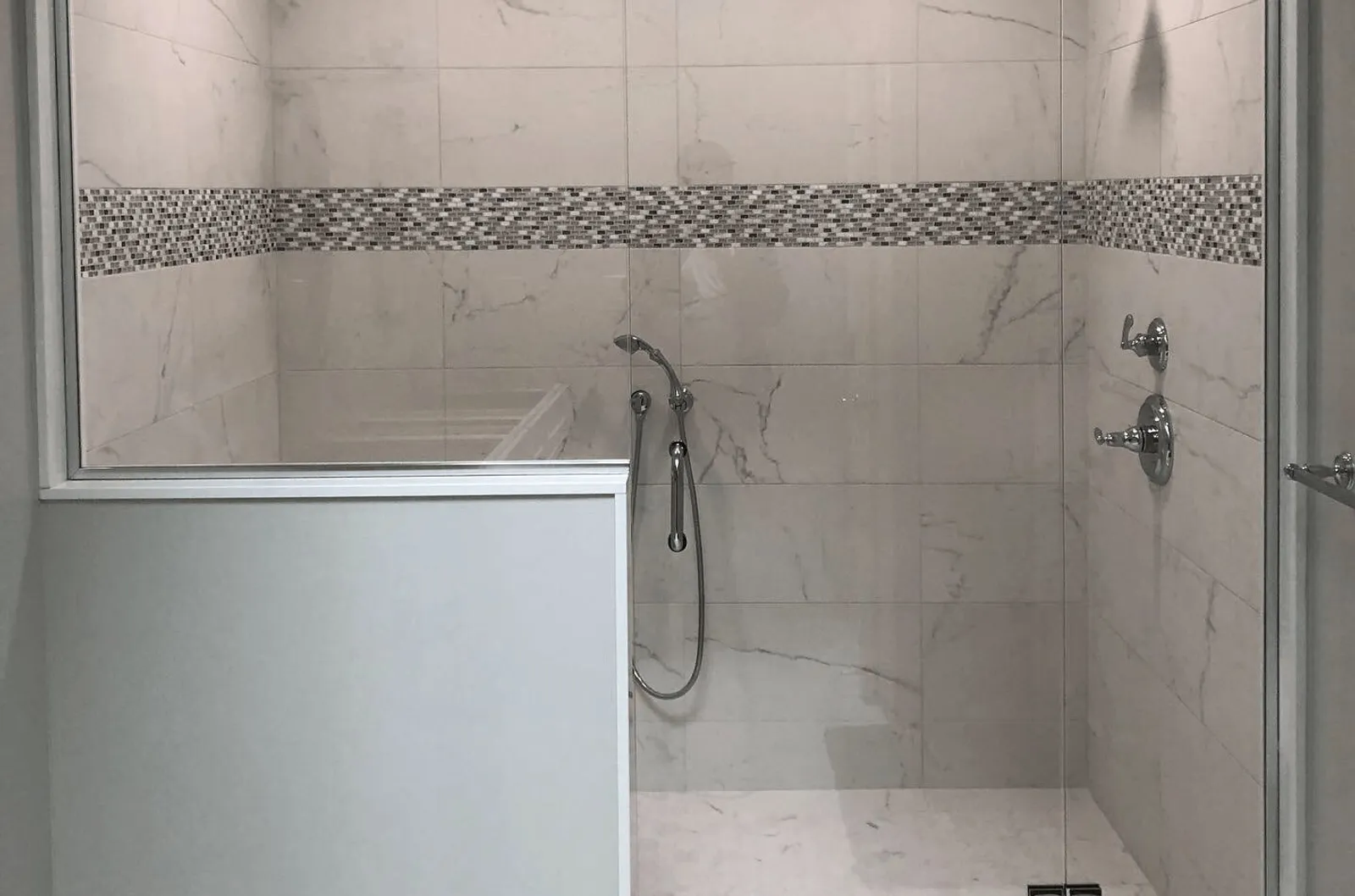 Glass shower panel on a half wall with a mosaic tile accent